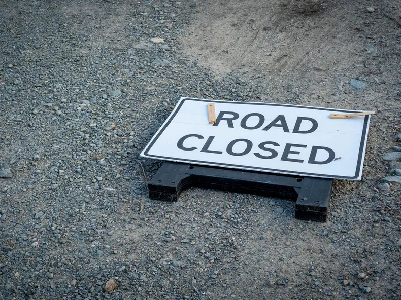 A road closed sign lies on a gravel pathway