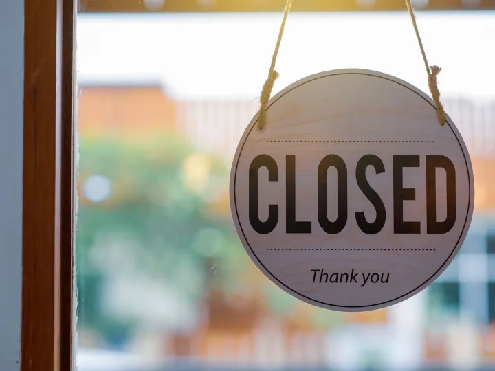 A wooden Closed sign hanging in a shop window