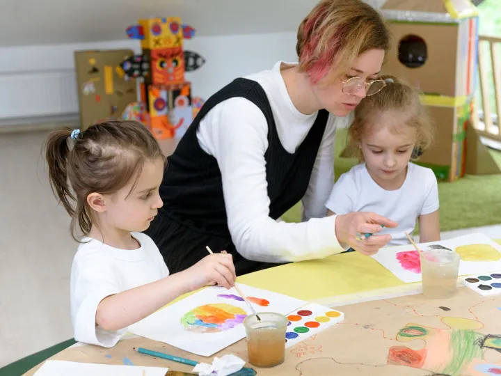 Early years practitioner helping two children with a watercolour painting activity
