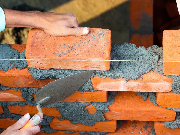 Builder laying a course of bricks with a trowel and string line