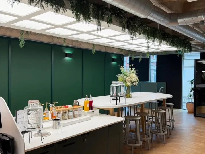 Office tea point with deep green panelled walls, a white worktop drinks station and a high table with stools