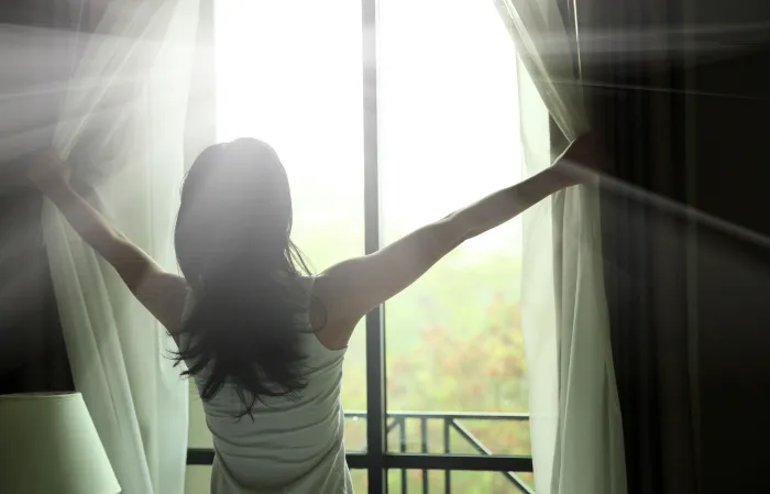 woman opening curtains at window