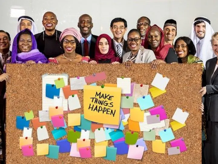 A diverse group of people behind a noticeboard of sticky notes headed Make things happen