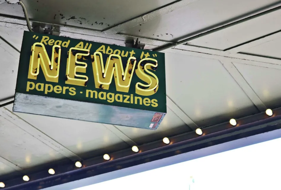 From below of illuminated signboard with news papers magazines inscriptions hanging on metal ceiling on street