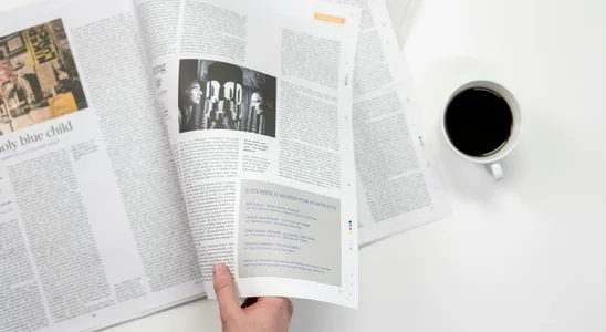 A close-up shot of a hand holding a newspaper with a coffee cup on a white surface.