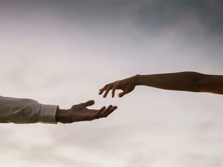 Two hands reaching towards each other against a soft twilight sky symbolizing connection and love.