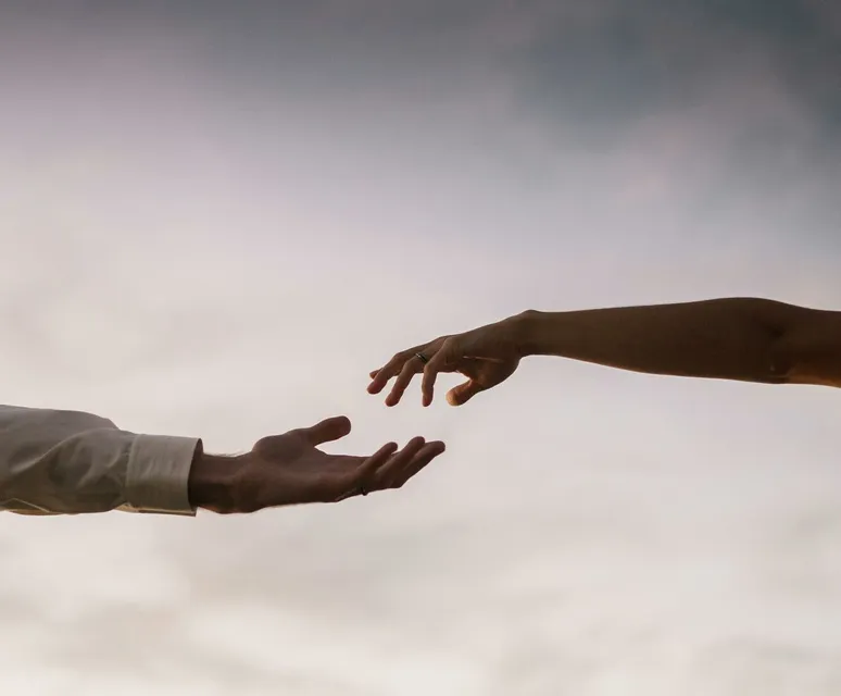 Two hands reaching towards each other against a soft twilight sky symbolizing connection and love.