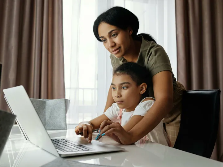 A mother helps her daughter with an online lesson on a laptop, showcasing family bonding and education at home.