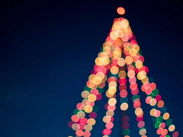 Colorful bokeh lights forming a Christmas tree against a dark blue sky.