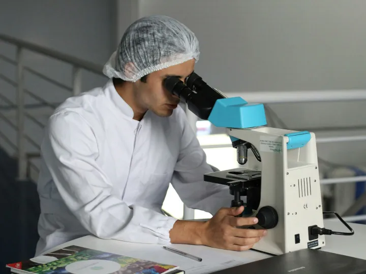 Scientist in a lab coat using a microscope to conduct research, focusing on healthcare improvements.