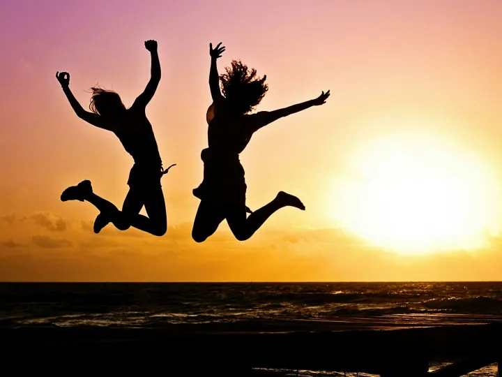 Silhouettes of two people joyfully jumping on a beach during a vibrant sunset.