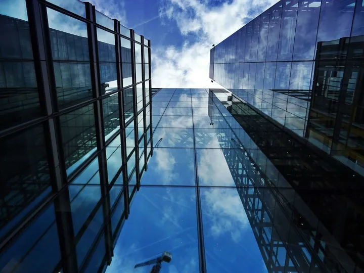 Perspective view of modern skyscraper facades with glass reflections of clouds and sky.