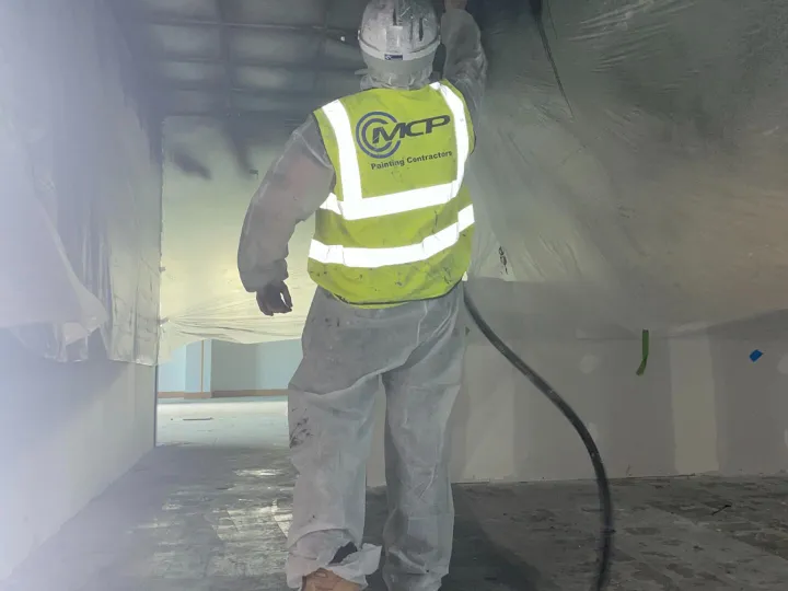 Construction worker wearing hi-vis jacket spraying surface