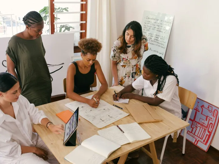 Diverse team collaborates on a project using digital and paper resources in a bright office.