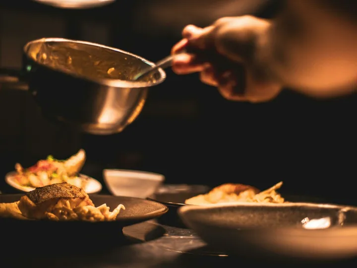 Gourmet dish being plated by a chef in a dimly lit restaurant's kitchen.