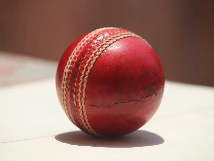 Detailed close-up of a red leather cricket ball showing wear and stitching.