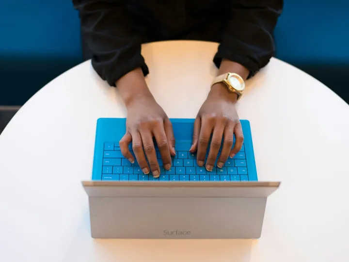 Hands of a person typing on a laptop with a blue k
