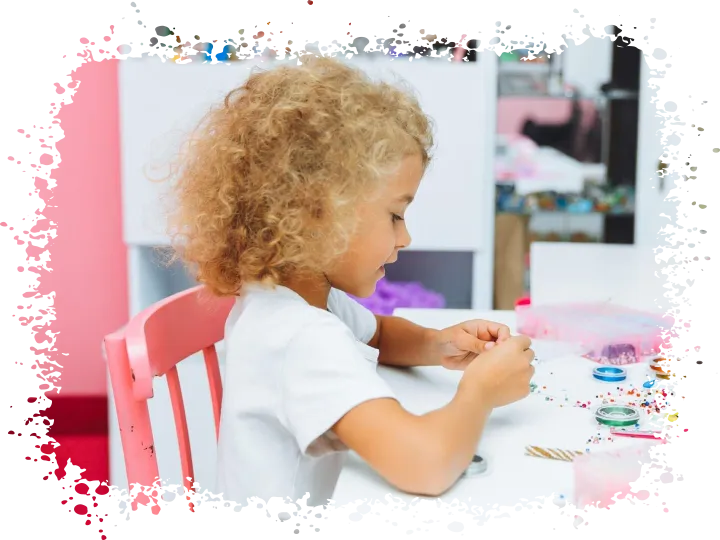 Cute little blonde girl making bead jewelry at a table in th