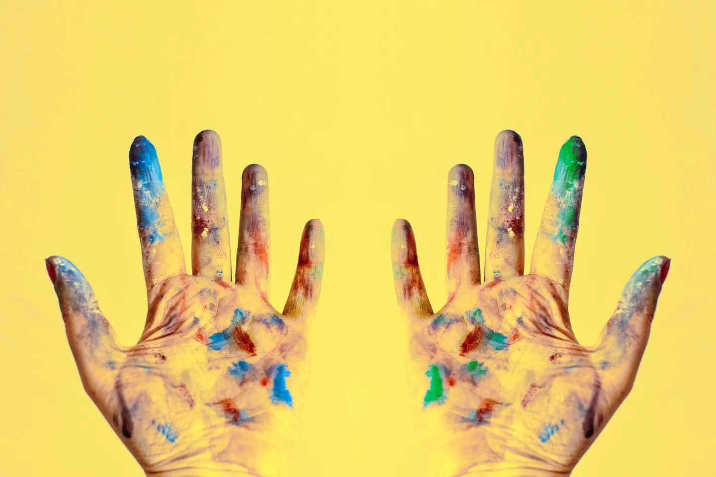 A child's paint-covered hands raised against a yellow background