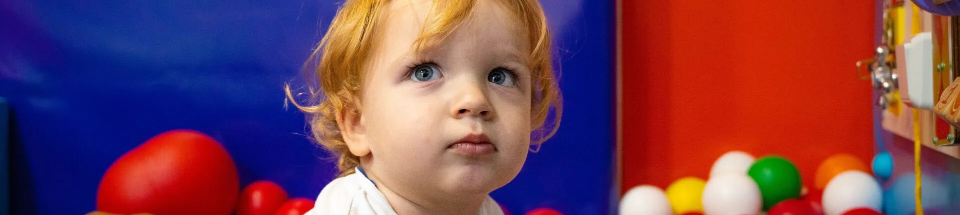 Toddler sitting in a colourful soft play ball pit
