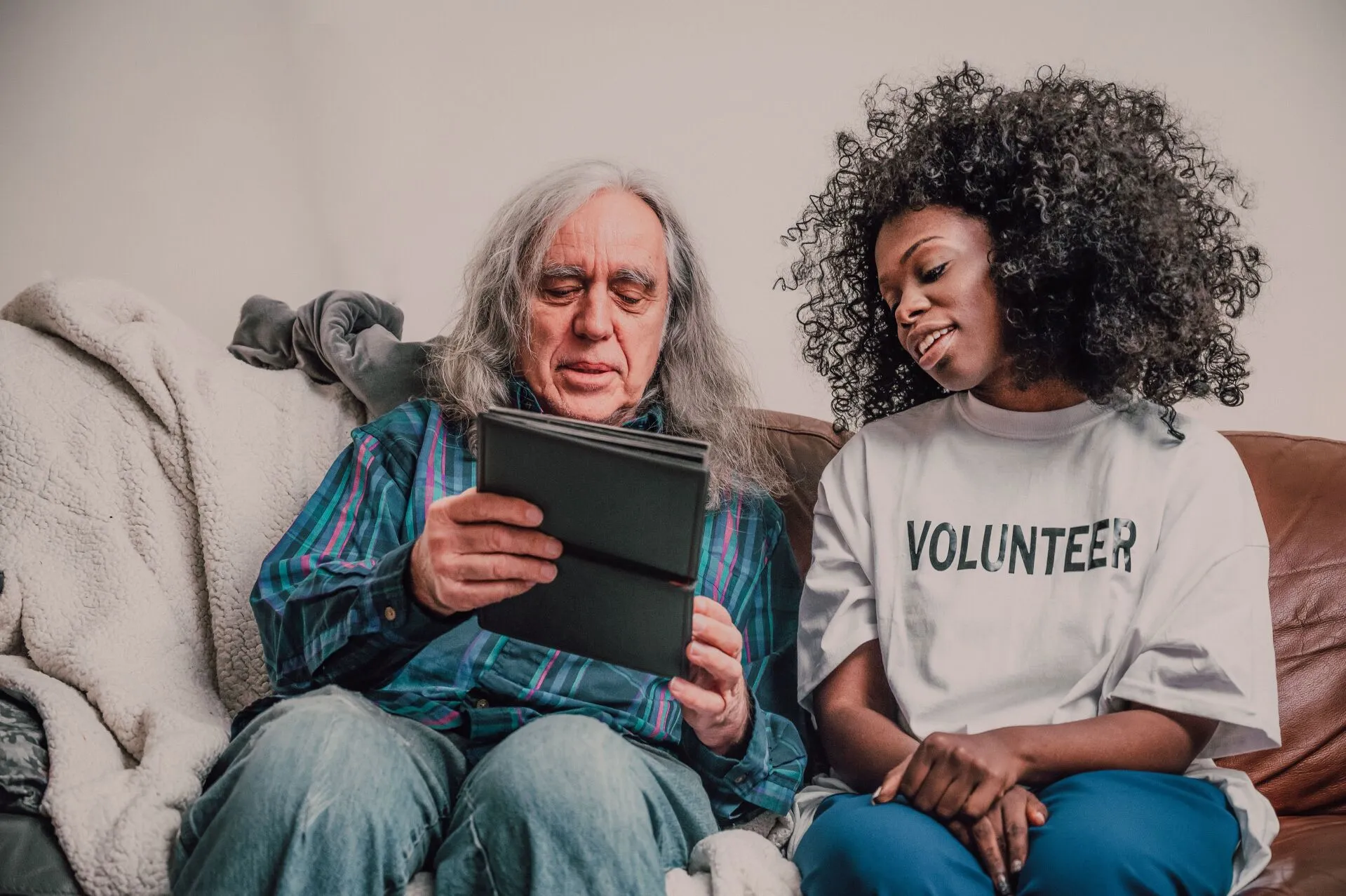 Young volunteer helping an older man use a tablet