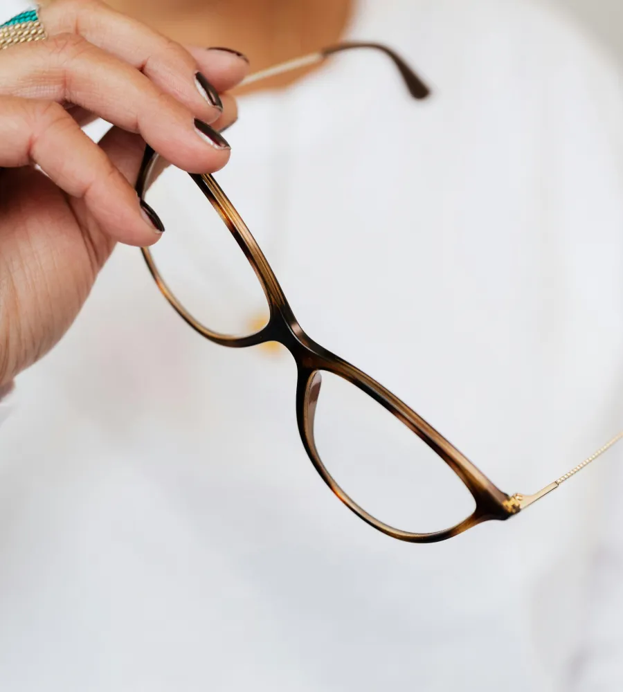 Crop unrecognizable elegant woman in white sweater and trendy optical glasses with brown frames and golden temples in hand