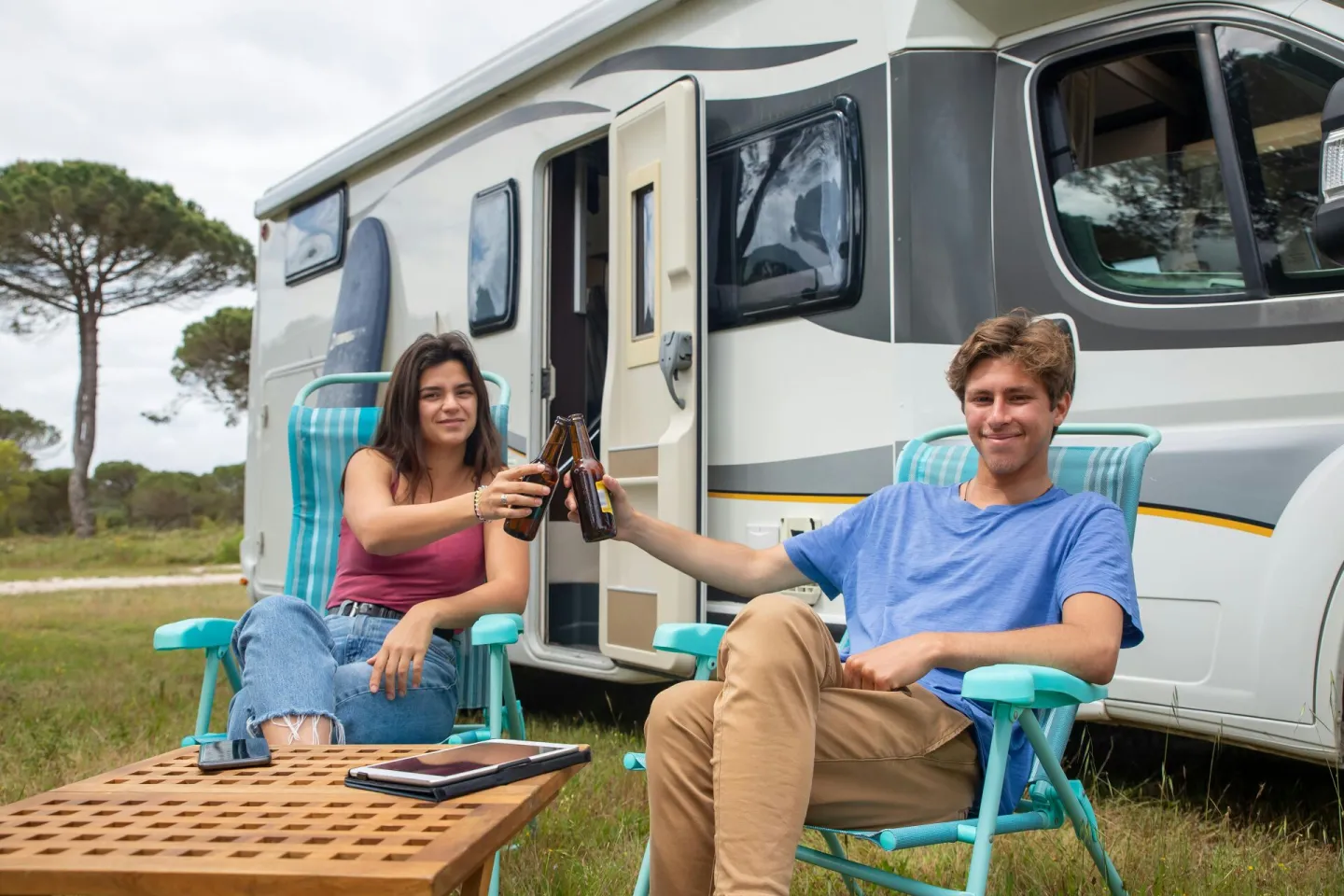 Happy couple clinking beer bottles outside camper