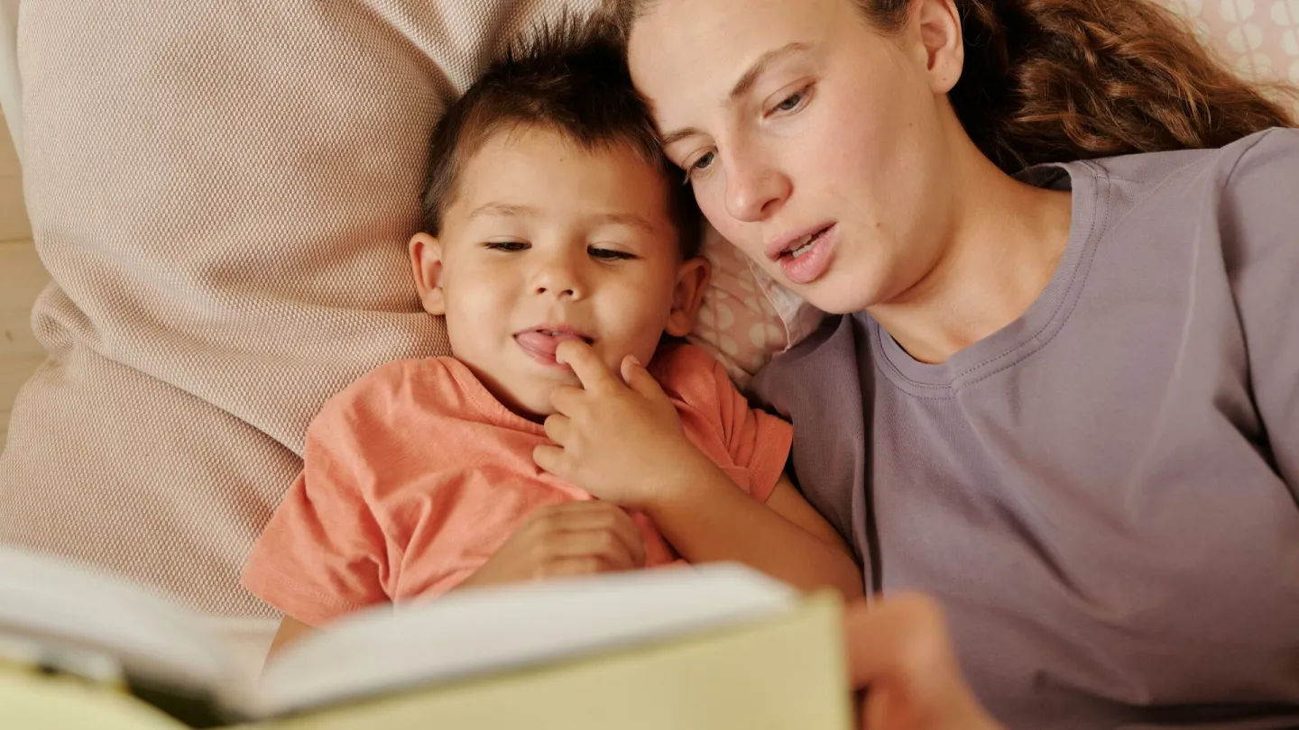 A loving mother and her young son enjoy reading a book together in bed. Captured in a cozy home setting.