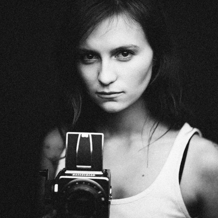 Black and white portrait of a woman holding a vintage camera, conveying classic elegance.