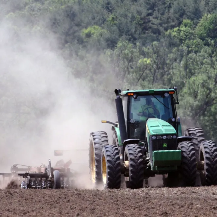 A green tractor plowing a field, creating clouds