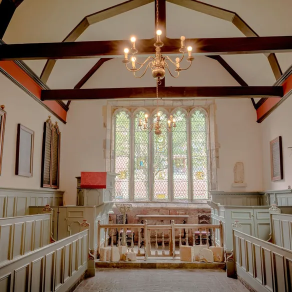 A warm chapel interior with red beams and a stained glass window