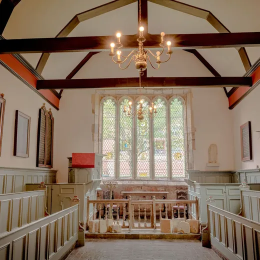 A warm chapel interior with red beams and a stained glass window