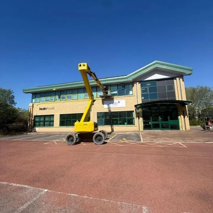 Two-storey brick office with green window frames and a yellow boom lift raised to the upper windows