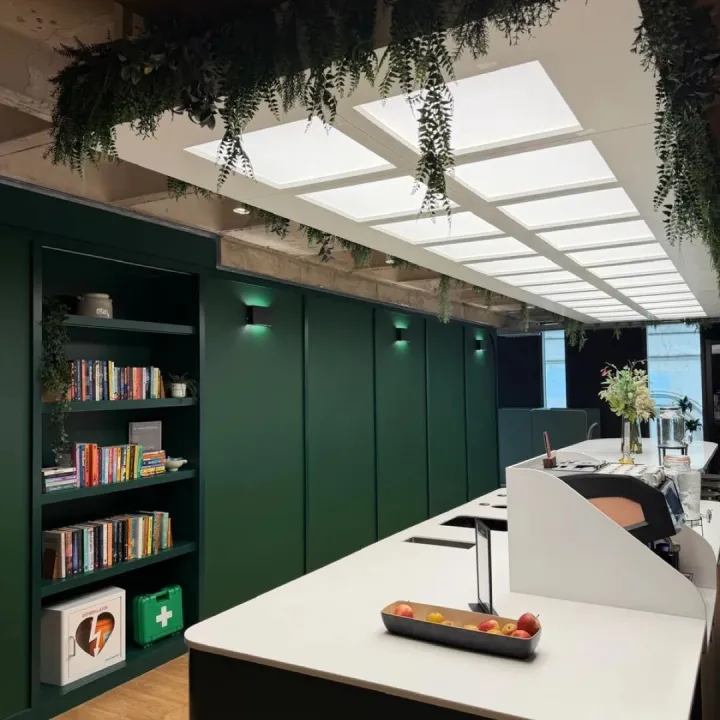 Deep green panelled wall with bookshelves and wall lights beside a white kitchen island