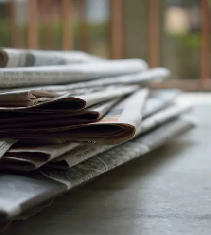 A close-up of a stack of newspapers resting on a desk, symbolizing information and media.