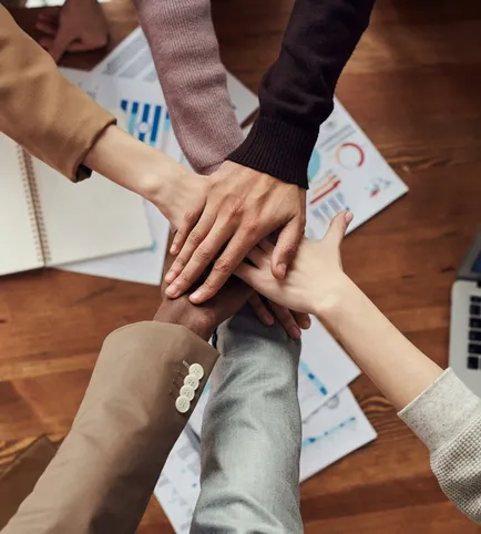 Diverse professionals unite for teamwork around a wooden table with laptops and documents.