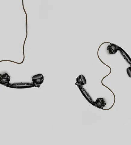 Two vintage black telephone handsets connected by cords on gray background.
