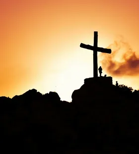 Majestic silhouette of a cross on a hill during a vivid sunset, symbolizing spirituality.