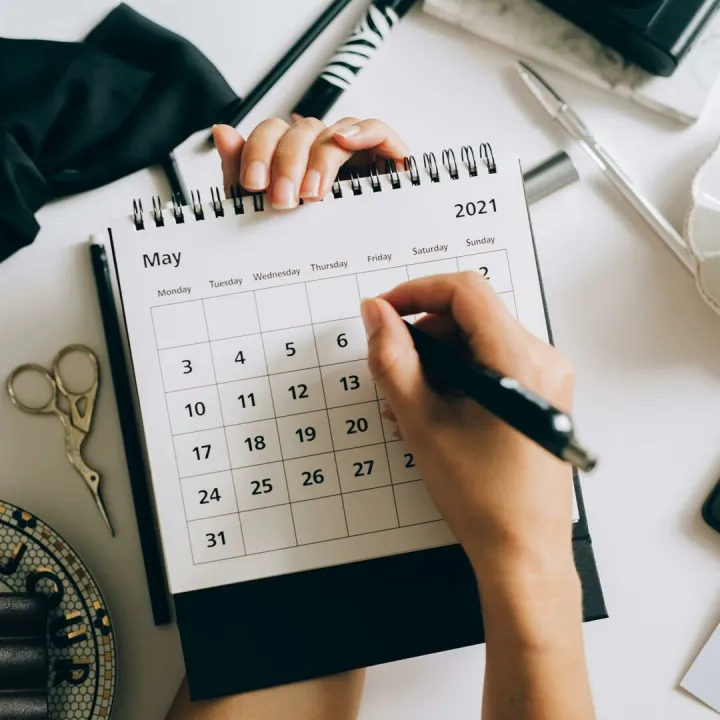 Top view of hands using a planner with coffee and accessories, focused on May 2021 calendar.
