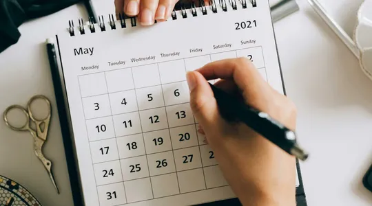 Top view of hands using a planner with coffee and accessories, focused on May 2021 calendar.