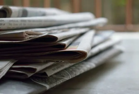 A close-up of a stack of newspapers resting on a desk, symbolizing information and media.