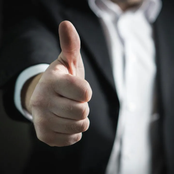 A close-up of a man's thumbs up gesture, symbo