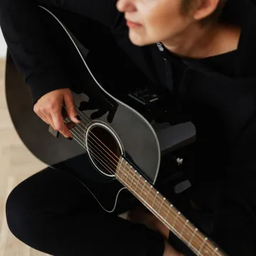 Person playing an acoustic guitar indoors, focusin