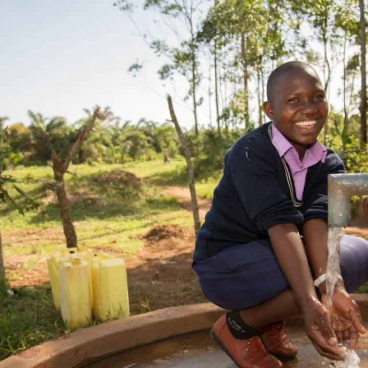 Prossy Nabiryo chair of St Balikddembe schools health club (SHC) using a new community water pump &ndash; Copyright All We Can