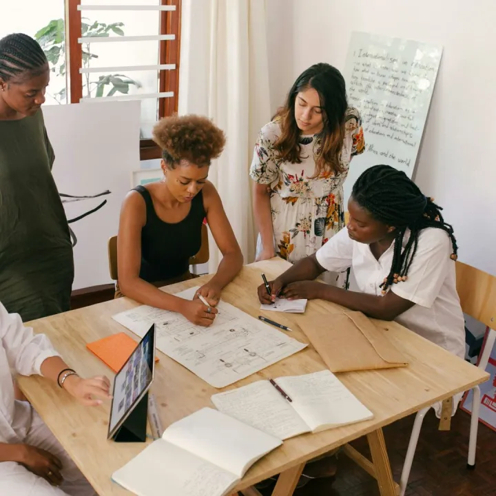 Diverse team collaborates on a project using digital and paper resources in a bright office.
