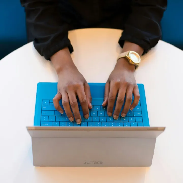 Hands of a person typing on a laptop with a blue k
