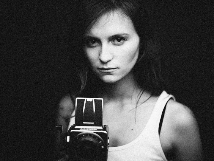 Black and white portrait of a woman holding a vintage camera, conveying classic elegance.