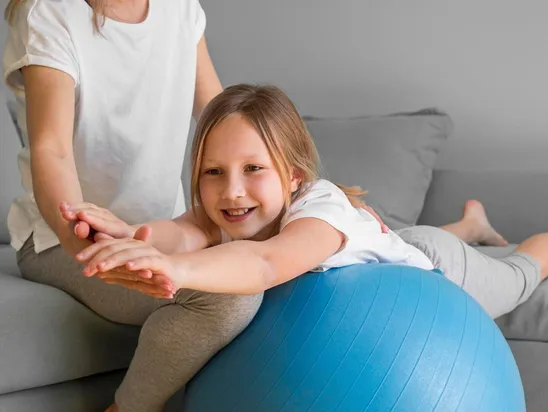 Mom helping girl to exercise on ball