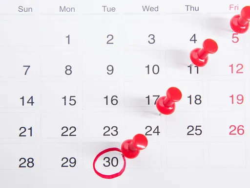 Close-up of a calendar with red push pins marking