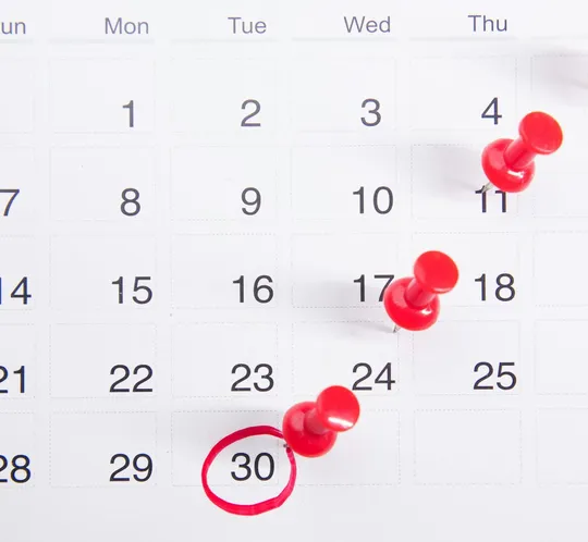 Close-up of a calendar with red push pins marking